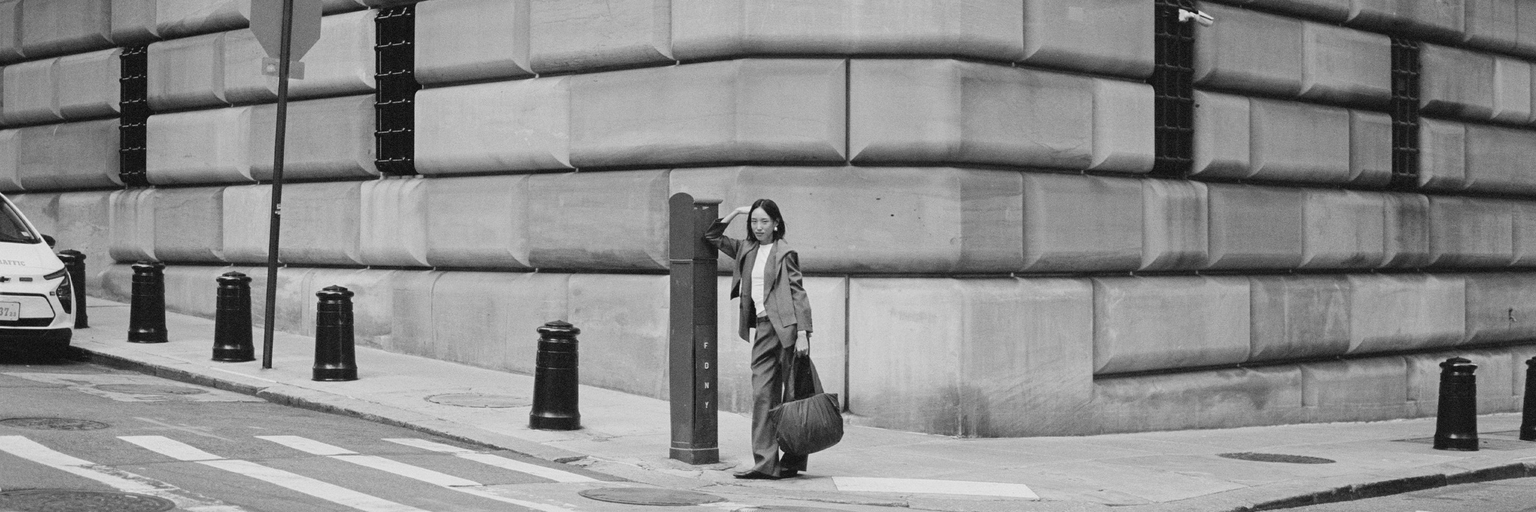 Woman with a TYVY tote bag standing on a city street next to a large building.