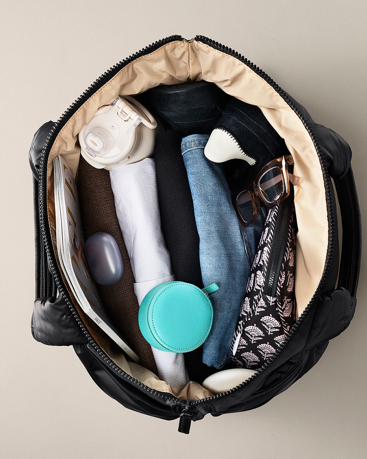 Open black bag with various items including clothes, a bottle, and a brush on a beige background. TYVY Aviator Tote bag optimized for travel.