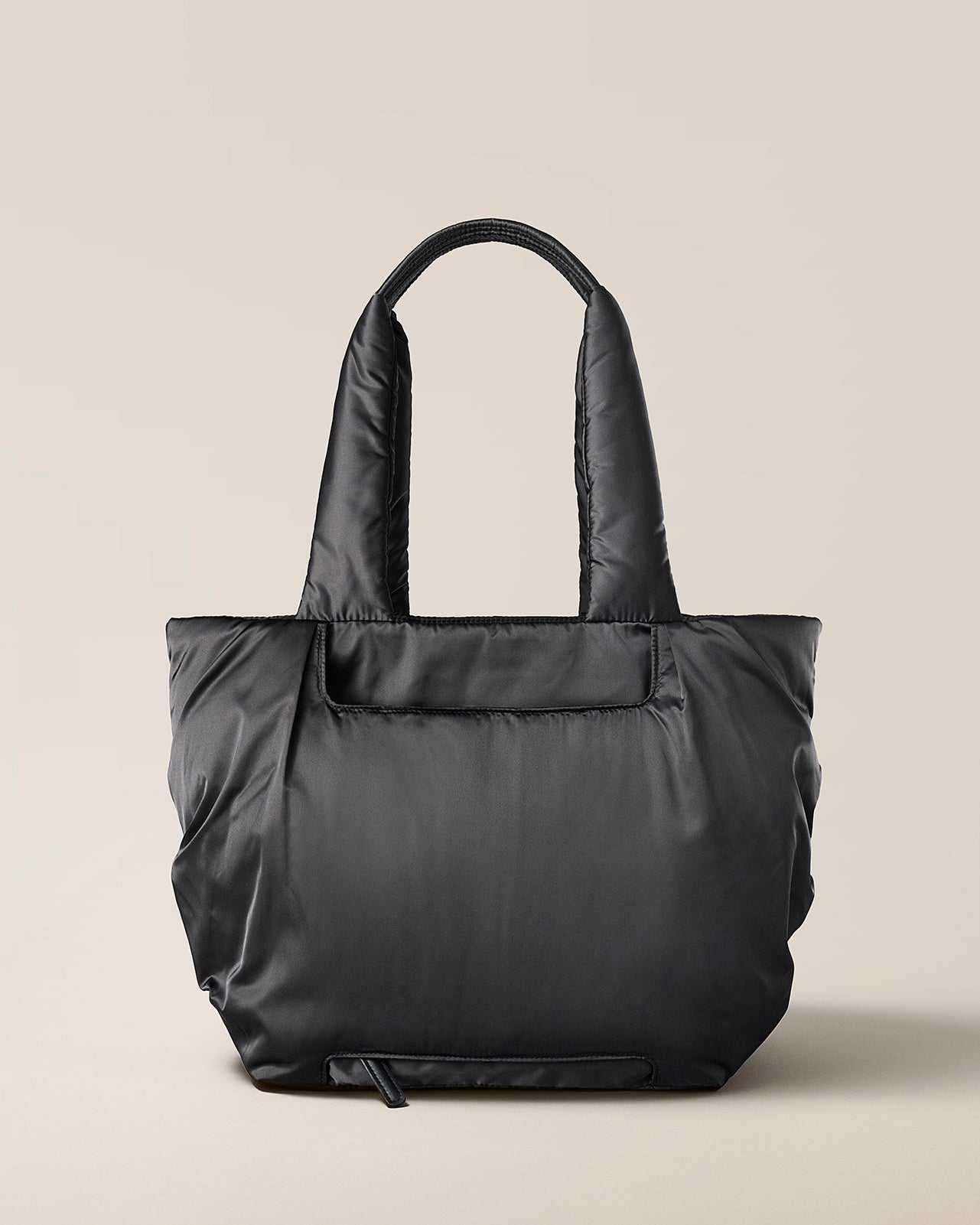 Black tote bag on a beige background. TYVY Aviator Tote bag optimized for travel.
