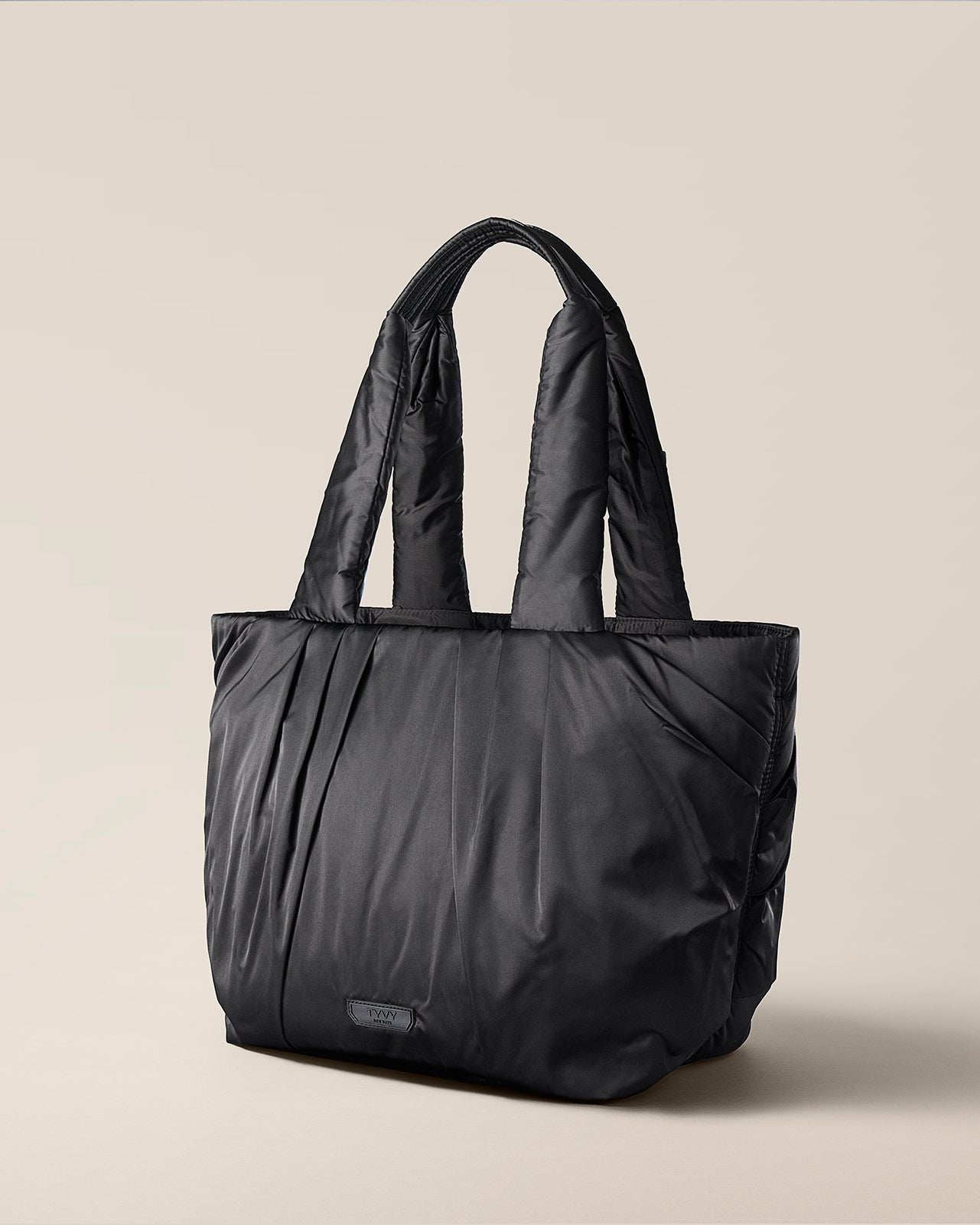 Black tote bag on a beige background. TYVY Aviator Tote bag optimized for travel.