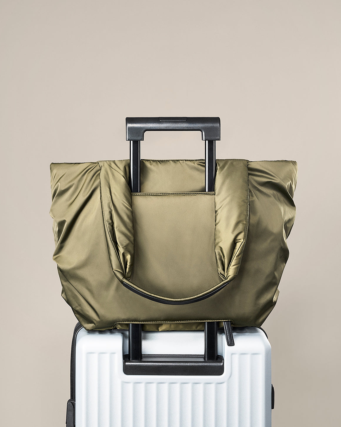 Green travel bag on top of a white suitcase against a beige background. TYVY Aviator Tote bag optimized for travel.
