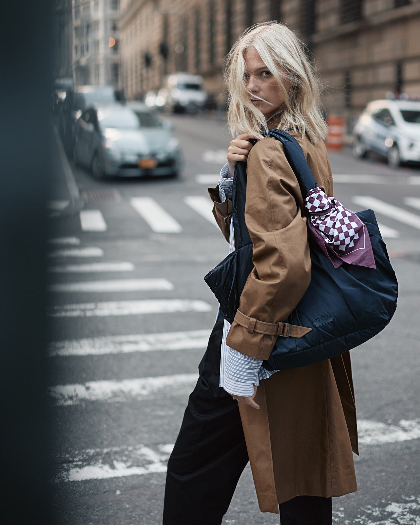 Woman walking on a city street with the black TYVY tote bag and checkered pattern scarf.