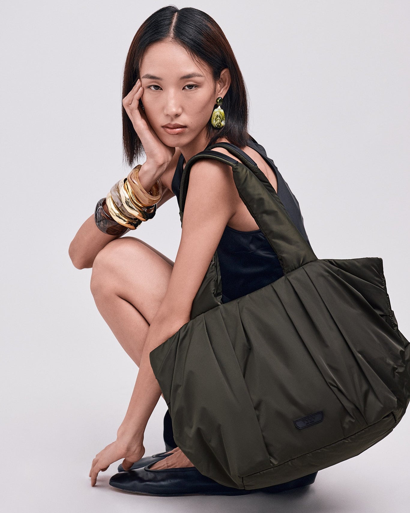 Woman holding a large olive green TYVY tote bag against a white background