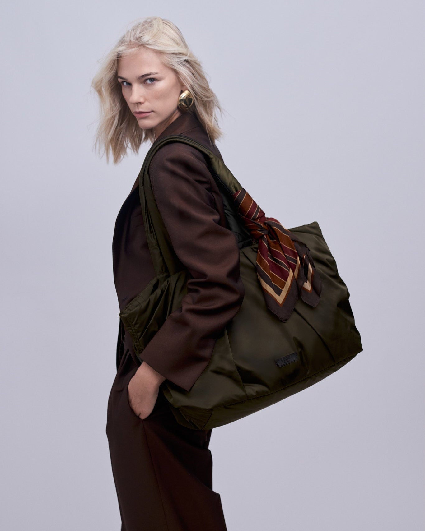 Woman carrying the large olive green tote bag with a plain background
