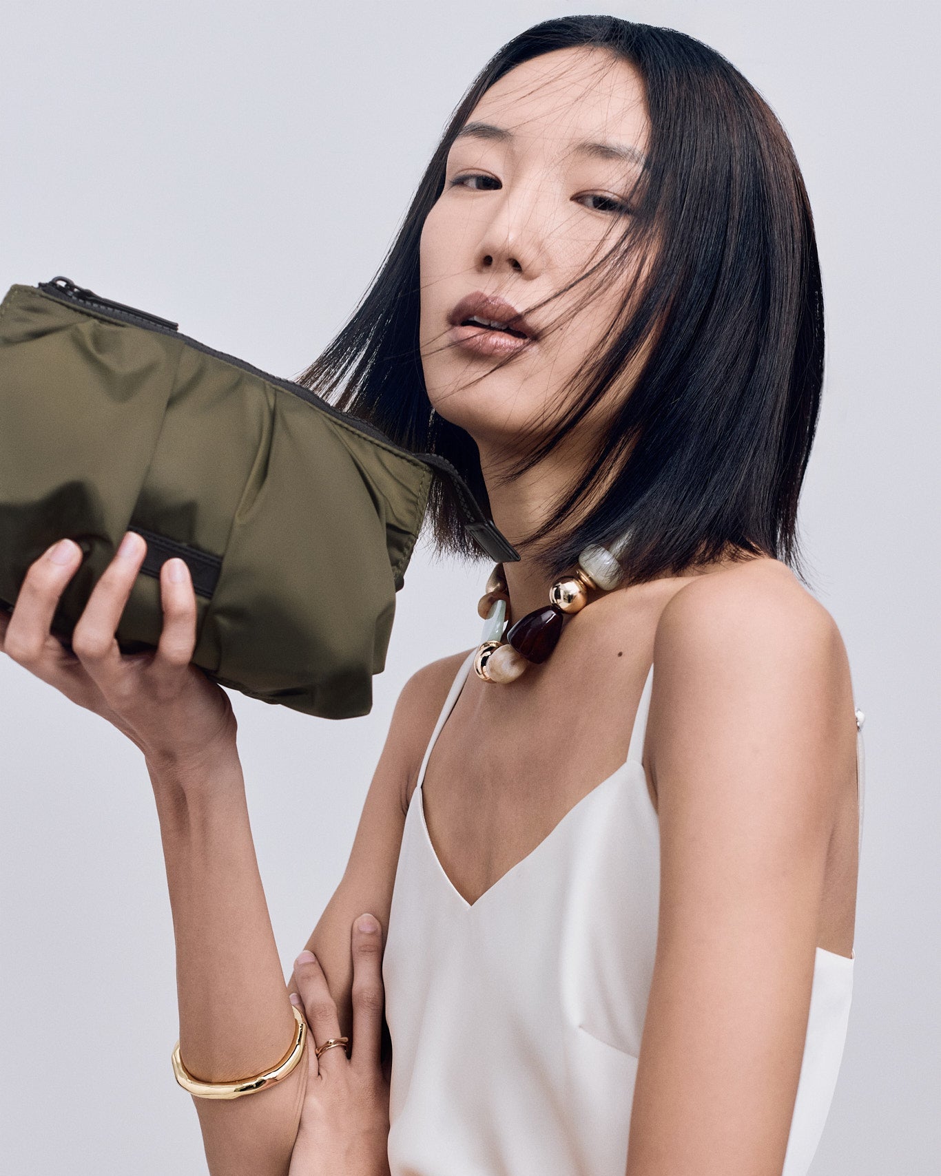 Woman holding an olive green TYVY pouch against a plain background